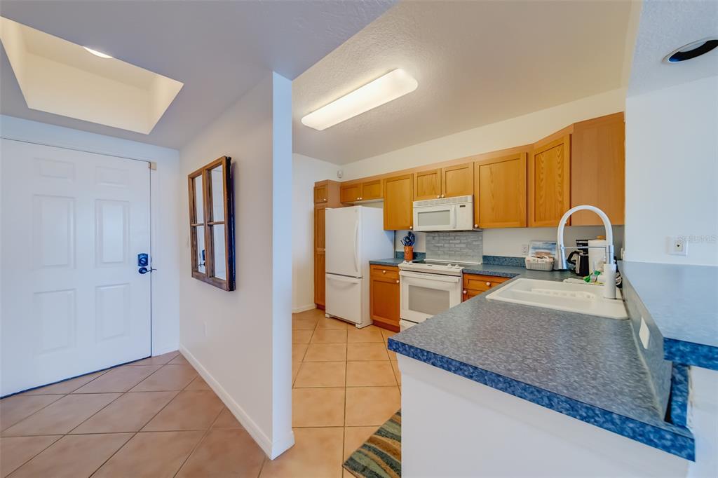 A kitchen with wood cabinets, white appliances, and blue countertops opens to a tiled entryway — 16550 GULF BOULEVARD UNIT 643, NORTH REDINGTON BEACH, FL