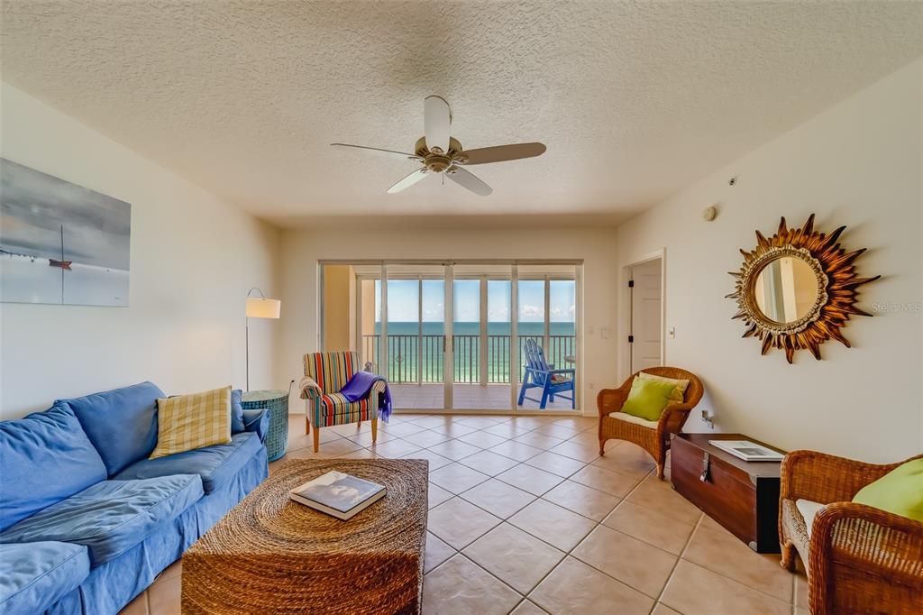 A living room with tile floors, a blue sofa, wicker chairs, and a balcony overlooking water — 16550 GULF BOULEVARD UNIT 643, NORTH REDINGTON BEACH, FL