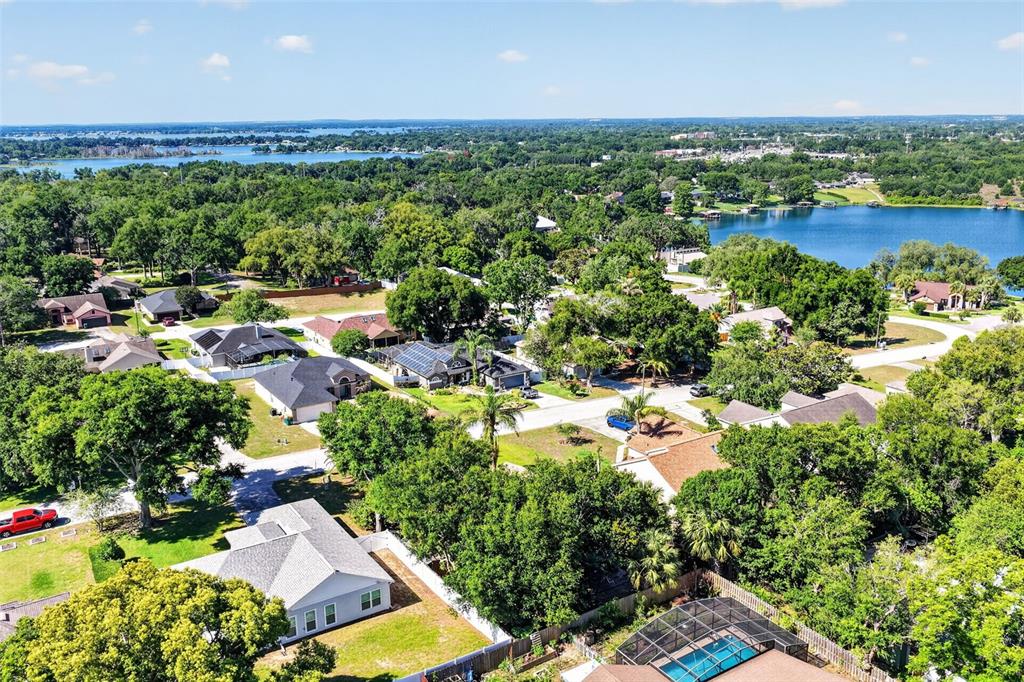 An aerial view shows suburban houses surrounded by dense trees near a large lake — 131 MADRONA DRIVE, EUSTIS, FL