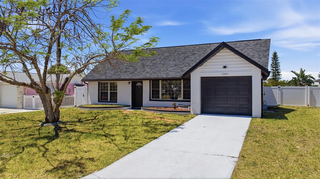 A single-story white brick house with a dark roof, garage, and a front lawn — 13615 GARRIS DRIVE, HUDSON, FL