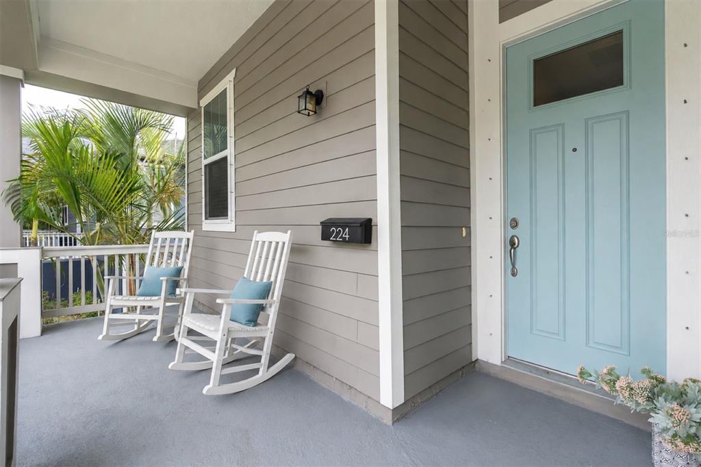 A covered front porch features two white rocking chairs, gray siding, and a light blue door — 224 NE JEFFERSON CIRCLE N, ST PETERSBURG, FL
