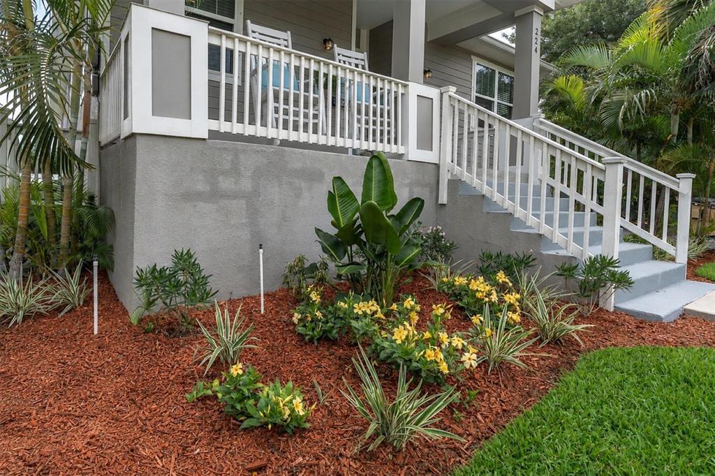 A raised front porch with white railings and stairs overlooks a garden with yellow flowers — 224 NE JEFFERSON CIRCLE N, ST PETERSBURG, FL
