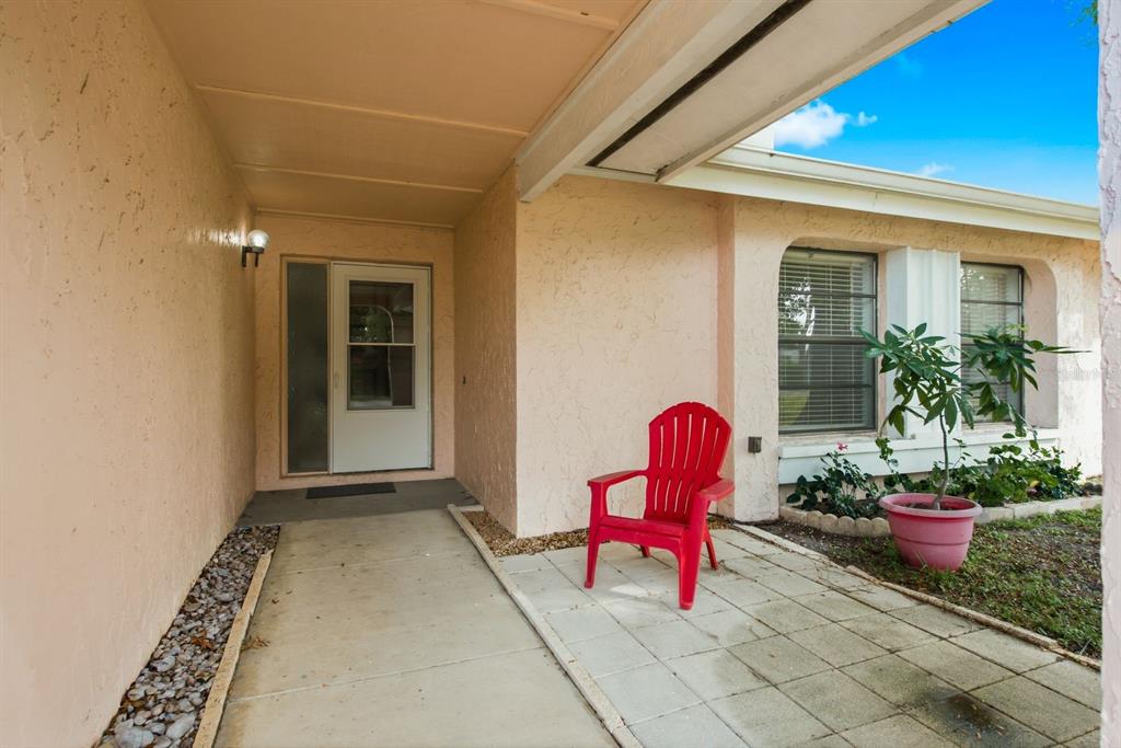A red chair sits on a concrete patio in front of a house entrance — 3916 LAKE ST GEORGE DRIVE, PALM HARBOR, FL