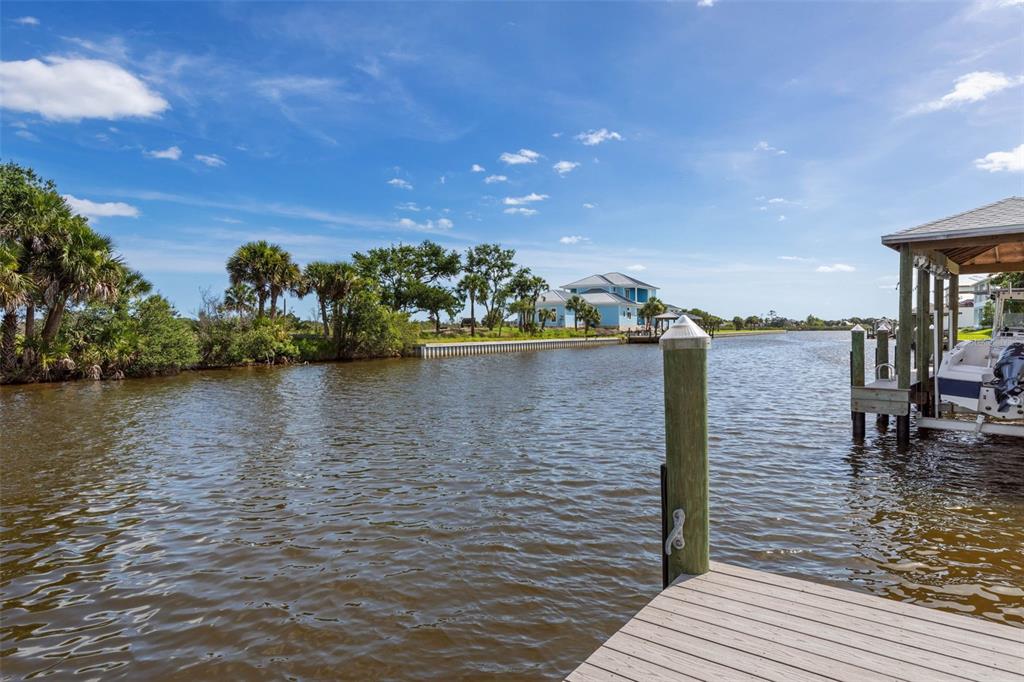 A wooden dock overlooks a canal with a boat lift and a distant house — 121 SEASIDE POINT, FLAGLER BEACH, FL