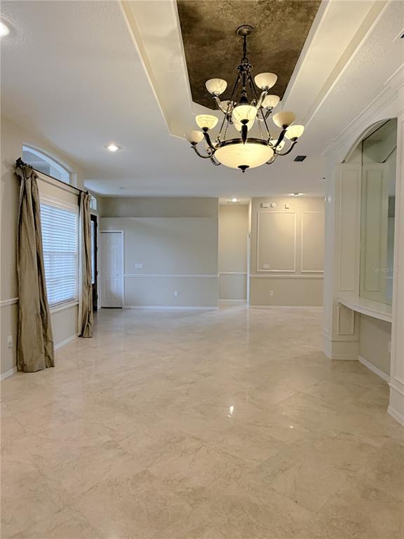 A spacious room features tile flooring, a tray ceiling with a chandelier, and beige walls — 3704 SWANS LANDING DRIVE, LAND O LAKES, FL