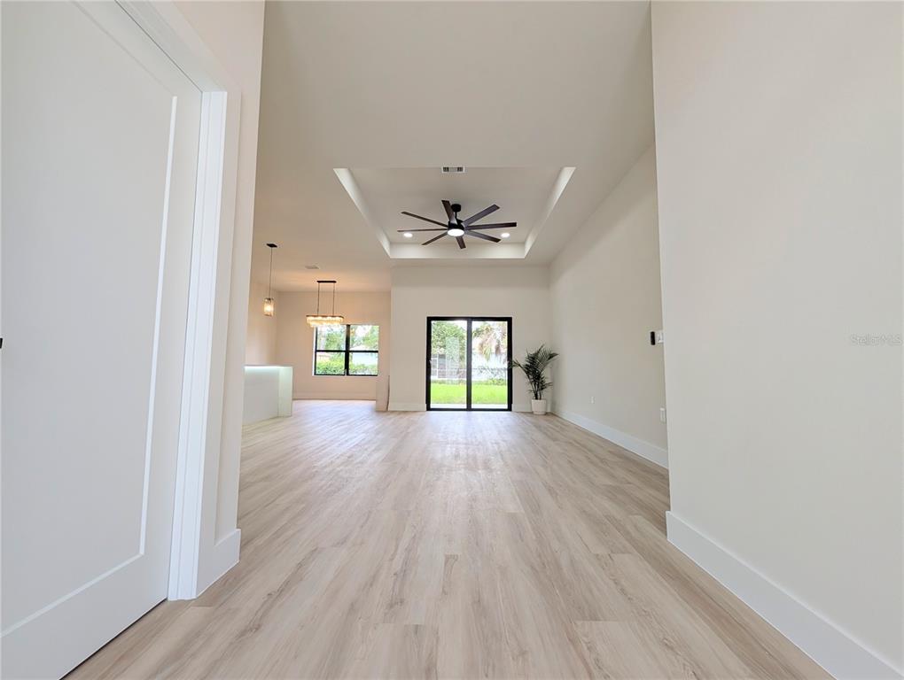A bright, open-concept living area features light wood-look flooring and a tray ceiling with fan — 7511 BLUTTER ROAD, NORTH PORT, FL
