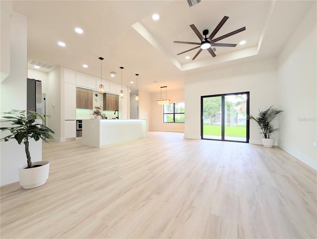 An open-concept living area features light wood flooring, a kitchen island, and a tray ceiling — 7511 BLUTTER ROAD, NORTH PORT, FL