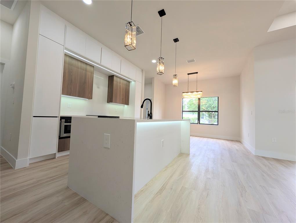 A modern kitchen features white cabinetry, wood-accented upper cabinets, a waterfall island, and pendant lighting — 7511 BLUTTER ROAD, NORTH PORT, FL