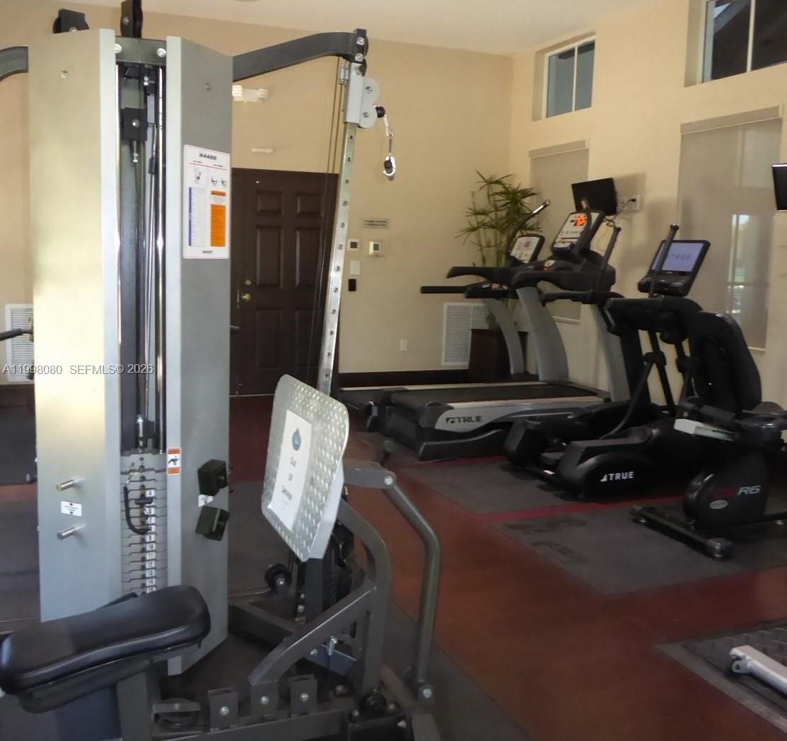 A fitness room features a weight machine, treadmills, and an exercise bike on wood flooring — 979 NE 42nd Ter, Homestead FL 33033, HOMESTEAD, FL