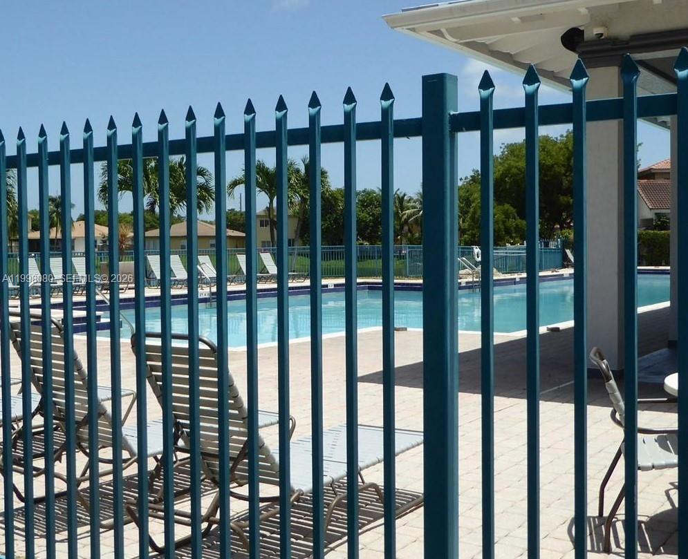 A blue metal fence stands in the foreground, overlooking a swimming pool and lounge chairs — 979 NE 42nd Ter, Homestead FL 33033, HOMESTEAD, FL