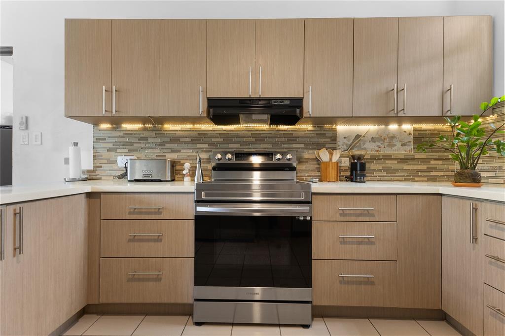 A kitchen features light wood cabinets, stainless steel appliances, and a horizontal glass tile backsplash — 5 HARBOUR LIGHTS, HUMACAO, PR
