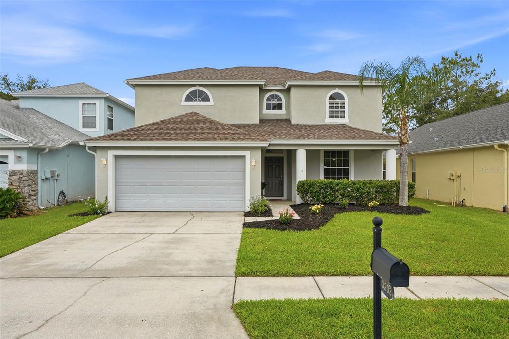 A two-story suburban house with a gray garage, light-colored stucco exterior, and a front lawn — 3203 SUNWATCH DRIVE, WESLEY CHAPEL, FL
