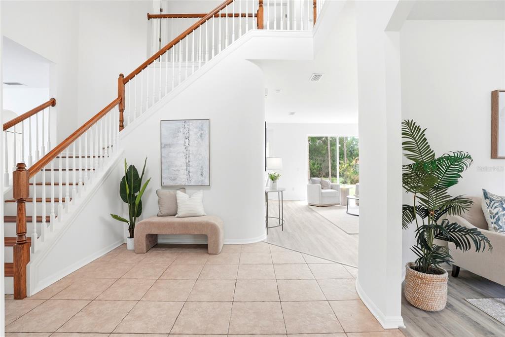 A tiled entryway features a curved staircase with wooden railings and a bench below — 3203 SUNWATCH DRIVE, WESLEY CHAPEL, FL