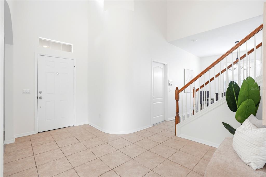 A bright entryway features tiled floors, a curved wall, and a wooden staircase with railings — 3203 SUNWATCH DRIVE, WESLEY CHAPEL, FL