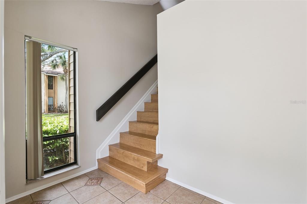 A staircase with wooden treads and a dark handrail sits beside a large window — 2901 CLUBVIEW DRIVE UNIT U1, ORLANDO, FL