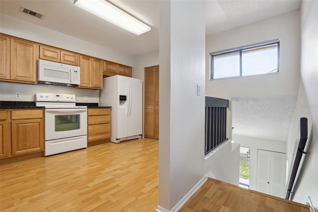 A kitchen with light wood cabinets and white appliances overlooks a staircase with a railing — 2901 CLUBVIEW DRIVE UNIT U1, ORLANDO, FL