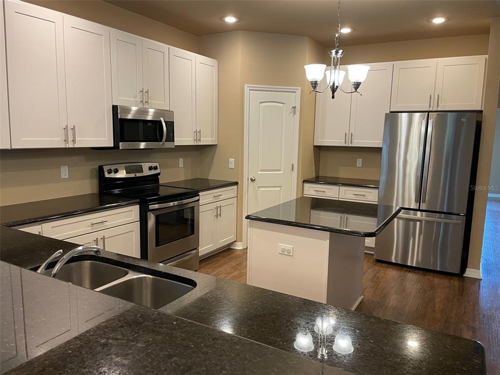 A kitchen features white cabinets, black countertops, stainless steel appliances, and a central island — 7879 SW 80TH DRIVE, GAINESVILLE, FL