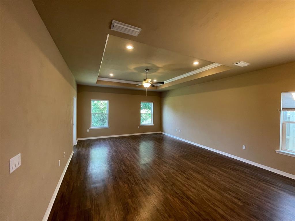 A spacious room with dark wood-look flooring, tan walls, and a recessed tray ceiling — 7879 SW 80TH DRIVE, GAINESVILLE, FL