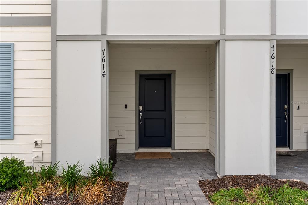 The exterior view shows two adjacent residential doorways with dark doors and paved walkways — 7614 OAK SPRING LANE, DAVENPORT, FL
