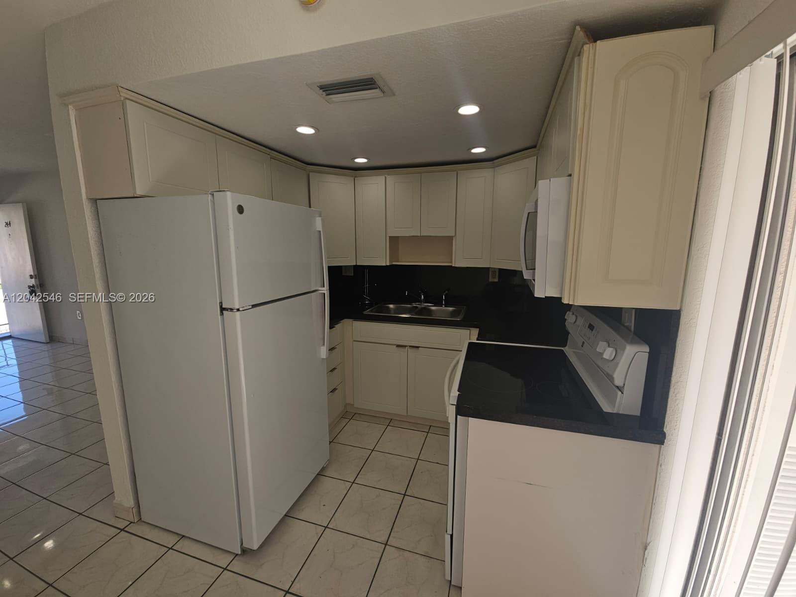 A small kitchen features white cabinets, black countertops, and white tile flooring — 1560 W 46th St # 244, Hialeah FL 33012, HIALEAH, FL