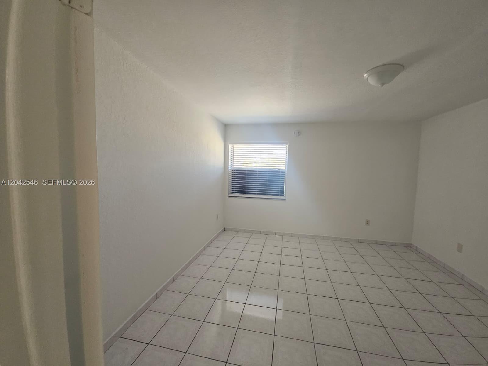 An empty room features white walls, light-colored tile flooring, and a single window with blinds — 1560 W 46th St # 244, Hialeah FL 33012, HIALEAH, FL