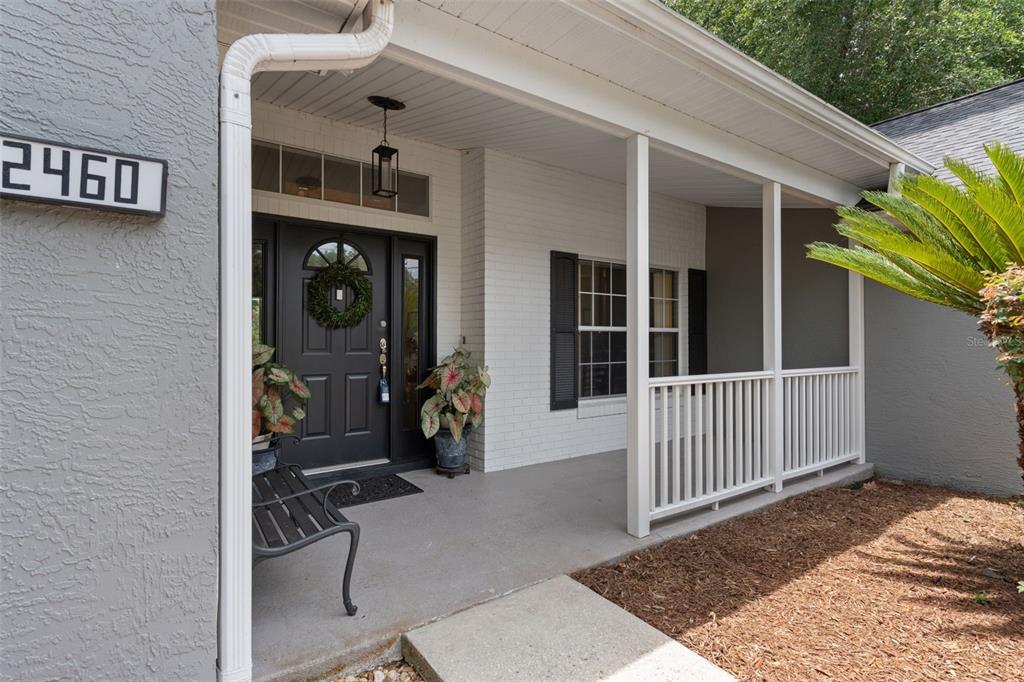 A covered front porch features a black door, white brick siding, and a white railing — 2460 W PINE RIDGE BOULEVARD, BEVERLY HILLS, FL