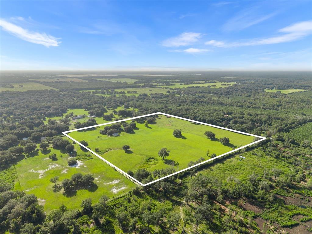 An aerial view shows a large, fenced-in grassy pasture surrounded by dense forest and trees — 360 & 390 SE 30TH AVENUE, TRENTON, FL