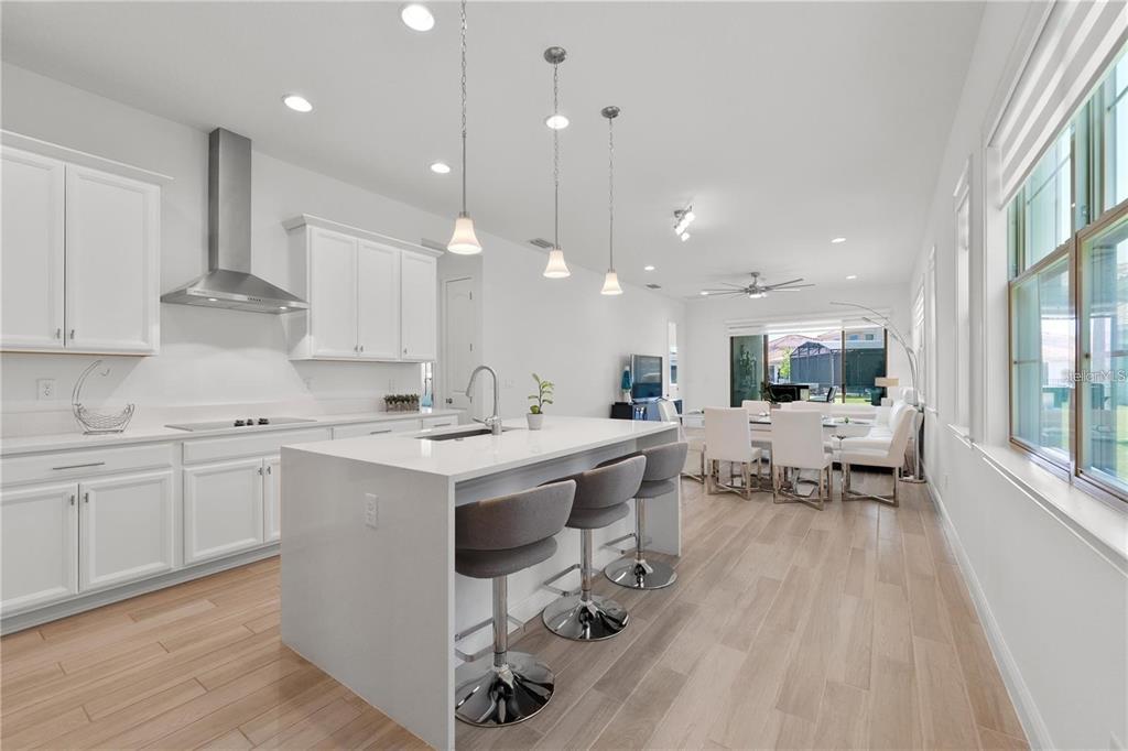 A modern kitchen features white cabinetry, a large quartz island with bar stools, and wood flooring — 13240 BROMBOROUGH DRIVE, ORLANDO, FL
