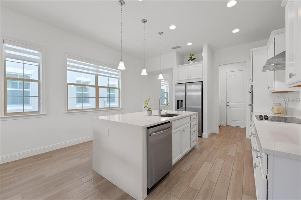 A modern kitchen features a white quartz island, stainless steel appliances, and light wood-look flooring — 13240 BROMBOROUGH DRIVE, ORLANDO, FL