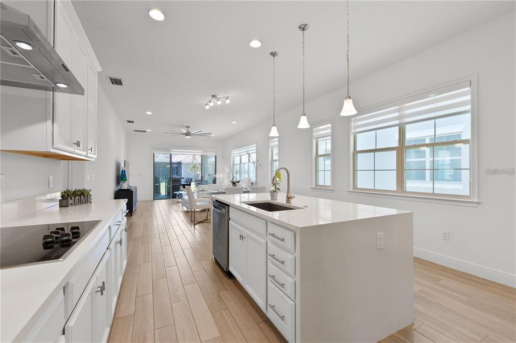 A bright, modern kitchen features white cabinetry, a quartz island, and light wood-look flooring — 13240 BROMBOROUGH DRIVE, ORLANDO, FL