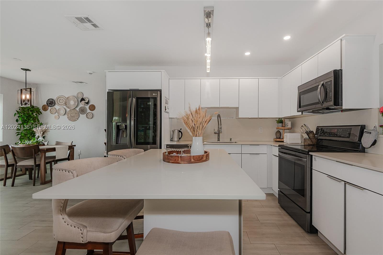 A modern kitchen features white cabinets, a central island, and stainless steel appliances — 1130 NE 143rd St, North Miami FL 33161, NORTH MIAMI, FL