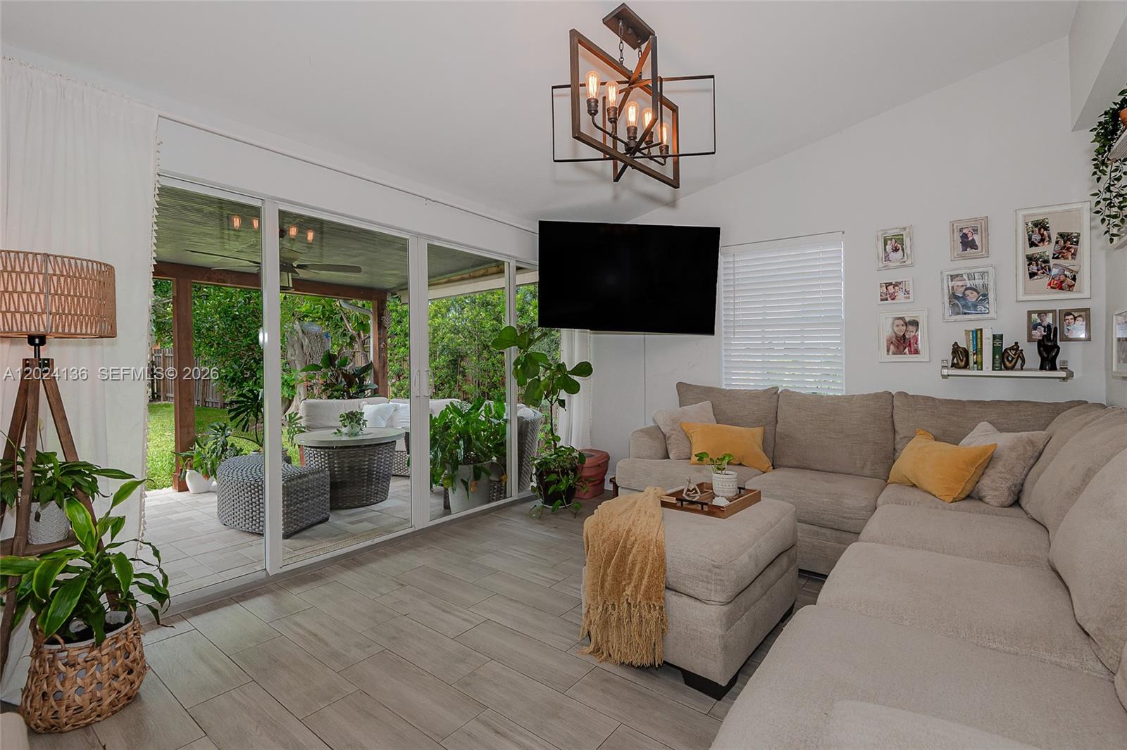 A living room features a sectional sofa, a wall-mounted television, and sliding doors to a patio — 1130 NE 143rd St, North Miami FL 33161, NORTH MIAMI, FL