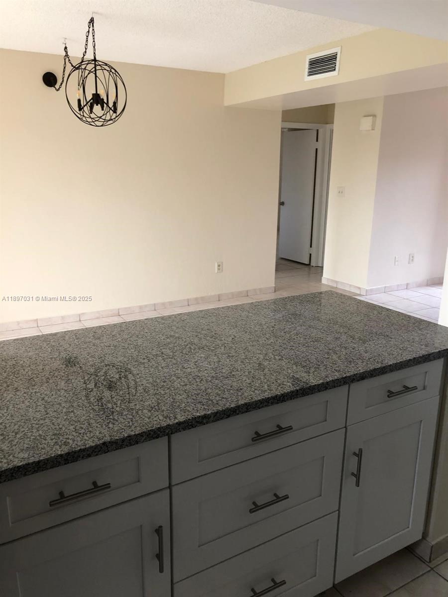 A kitchen island with gray cabinets and a granite countertop sits before a dining area — 8401 SW 107th Ave # 313E, Miami FL 33173, MIAMI, FL