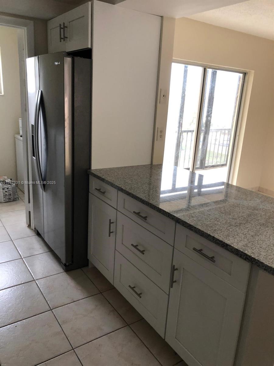 A kitchen features white cabinets, granite countertops, a stainless steel refrigerator, and tiled flooring — 8401 SW 107th Ave # 313E, Miami FL 33173, MIAMI, FL
