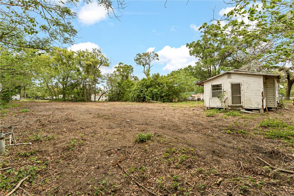 A small, weathered white wooden shed sits on a cleared, dirt-covered lot with surrounding trees — 40611 OTIS ALLEN ROAD, ZEPHYRHILLS, FL