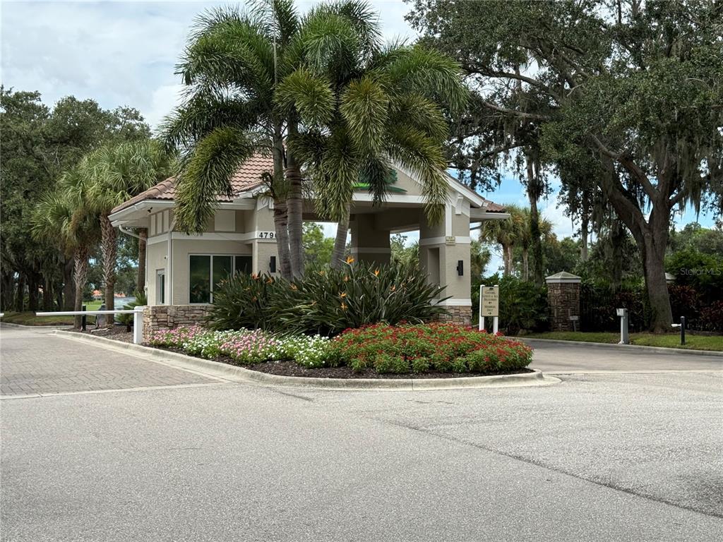 A gated community entrance features a guardhouse, palm trees, and a landscaped flower bed — 5251 MAHOGANY RUN AVENUE UNIT 524, SARASOTA, FL