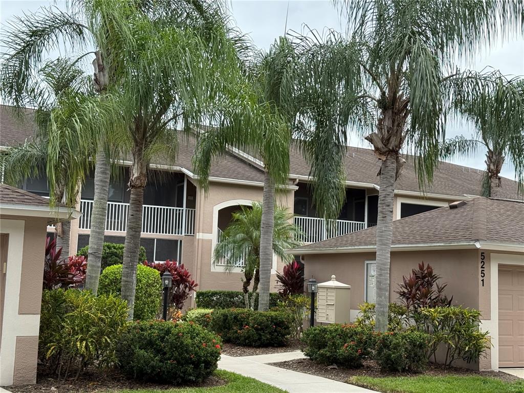 A multi-story apartment building exterior features palm trees, manicured landscaping, and a concrete walkway — 5251 MAHOGANY RUN AVENUE UNIT 524, SARASOTA, FL