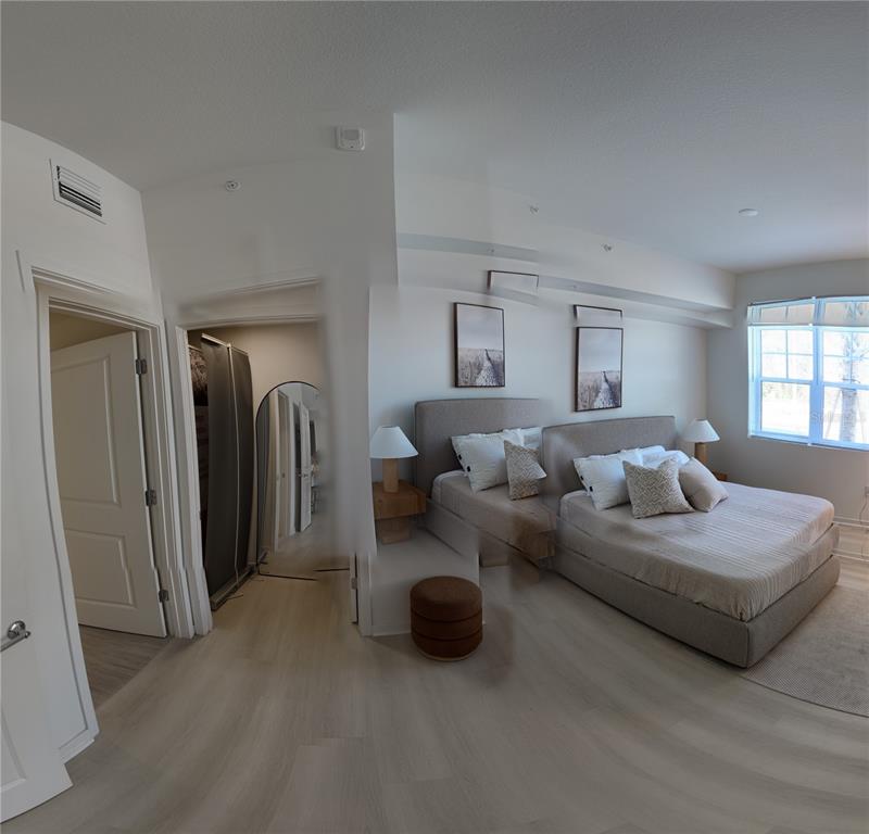 A bedroom features a light-colored bed, two framed wall prints, and a walk-in closet — 5587 MILLENIA PARK BLVD UNIT 218, ORLANDO, FL