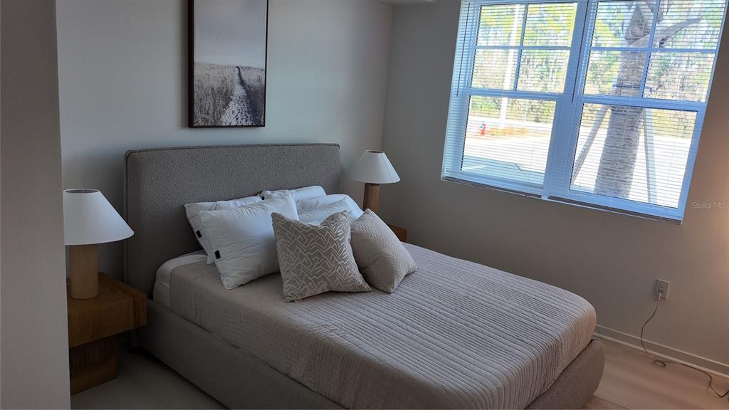 A bedroom features a gray upholstered bed, two bedside lamps, and a window with blinds — 5587 MILLENIA PARK BLVD UNIT 218, ORLANDO, FL