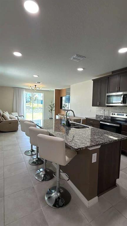 A kitchen with a granite island and bar stools opens into a living area — 1445 SEA GLASS ROAD, HAINES CITY, FL