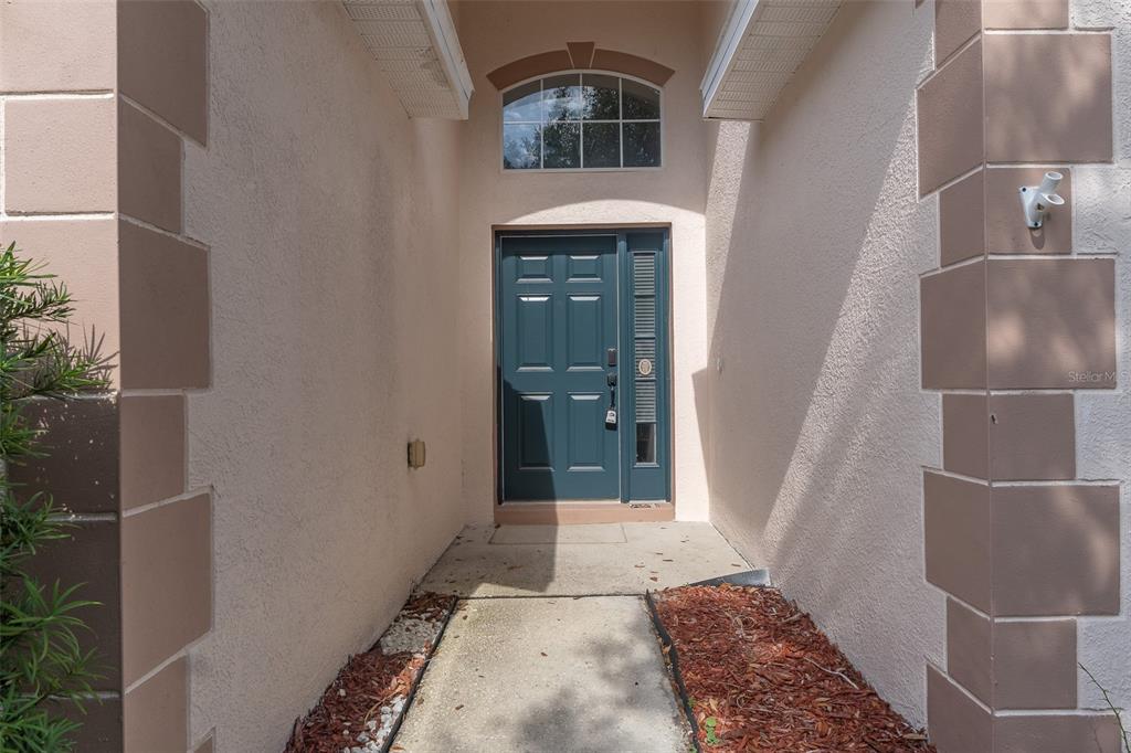 A teal front door with a sidelight is framed by a recessed entryway with stucco walls — 6806 GUILFORD CREST DRIVE, APOLLO BEACH, FL