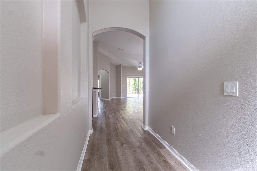 A hallway with light gray walls and wood-look flooring leads toward an arched entryway — 6806 GUILFORD CREST DRIVE, APOLLO BEACH, FL