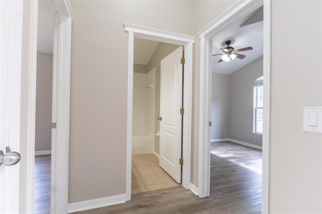 A hallway with light gray walls and wood-look flooring leads to a bathroom and bedroom — 6806 GUILFORD CREST DRIVE, APOLLO BEACH, FL