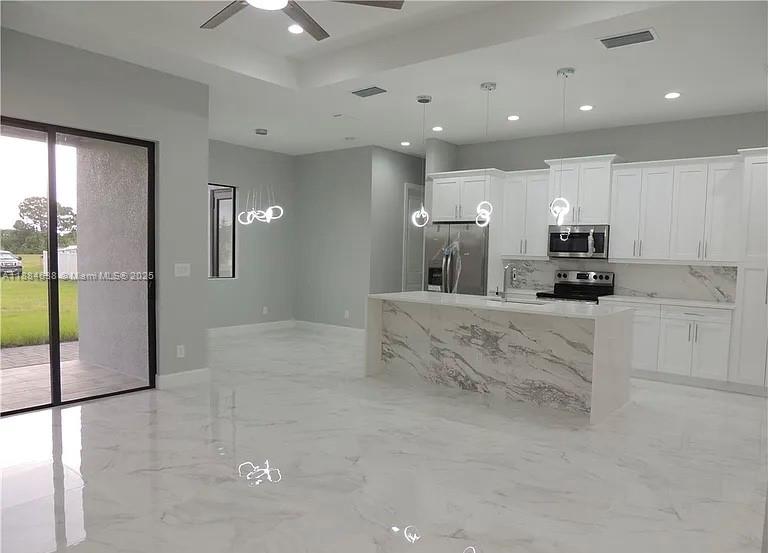 A modern kitchen features white cabinetry, a marble-topped island, and glossy tile flooring — 2011 NW 10 PL, Cape Coral FL 33993, CAPE CORAL, FL