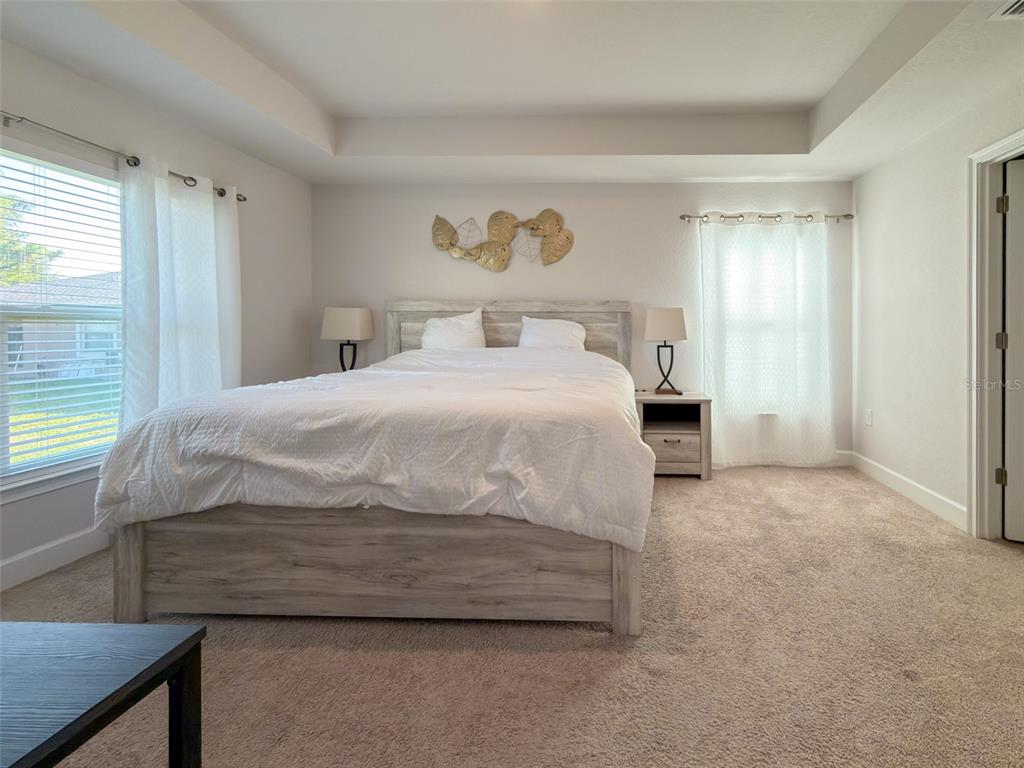 A bedroom features a light wood bed frame, white bedding, and two windows with curtains — 249 ROTONDA BOULEVARD W, ROTONDA WEST, FL