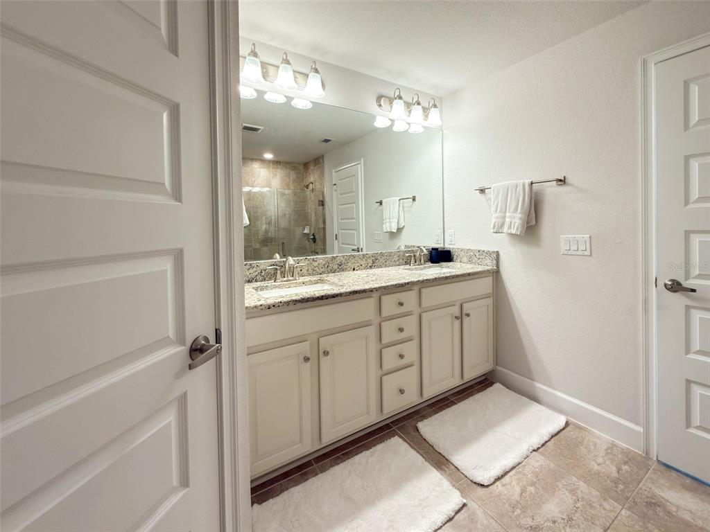 A bathroom features a double-sink vanity with granite countertops, a large mirror, and tiled flooring — 249 ROTONDA BOULEVARD W, ROTONDA WEST, FL