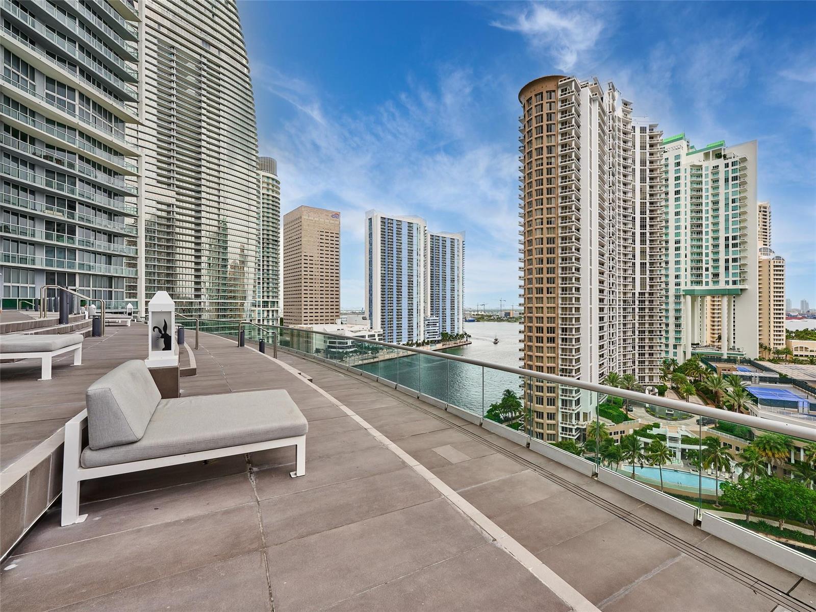 A high-rise balcony with lounge chairs overlooks a waterfront city skyline with multiple skyscrapers — 495 Brickell Avenue # 4506, Miami FL 33131, MIAMI, FL