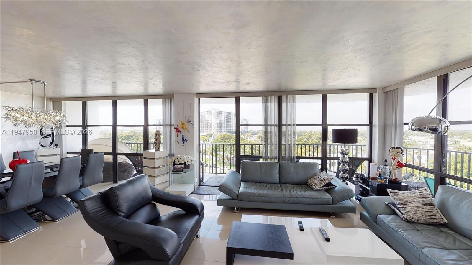A modern living and dining room features leather furniture, floor-to-ceiling windows, and a balcony view — 800 Parkview Dr # 709, Hallandale Beach FL 33009, HALLANDALE BEACH, FL