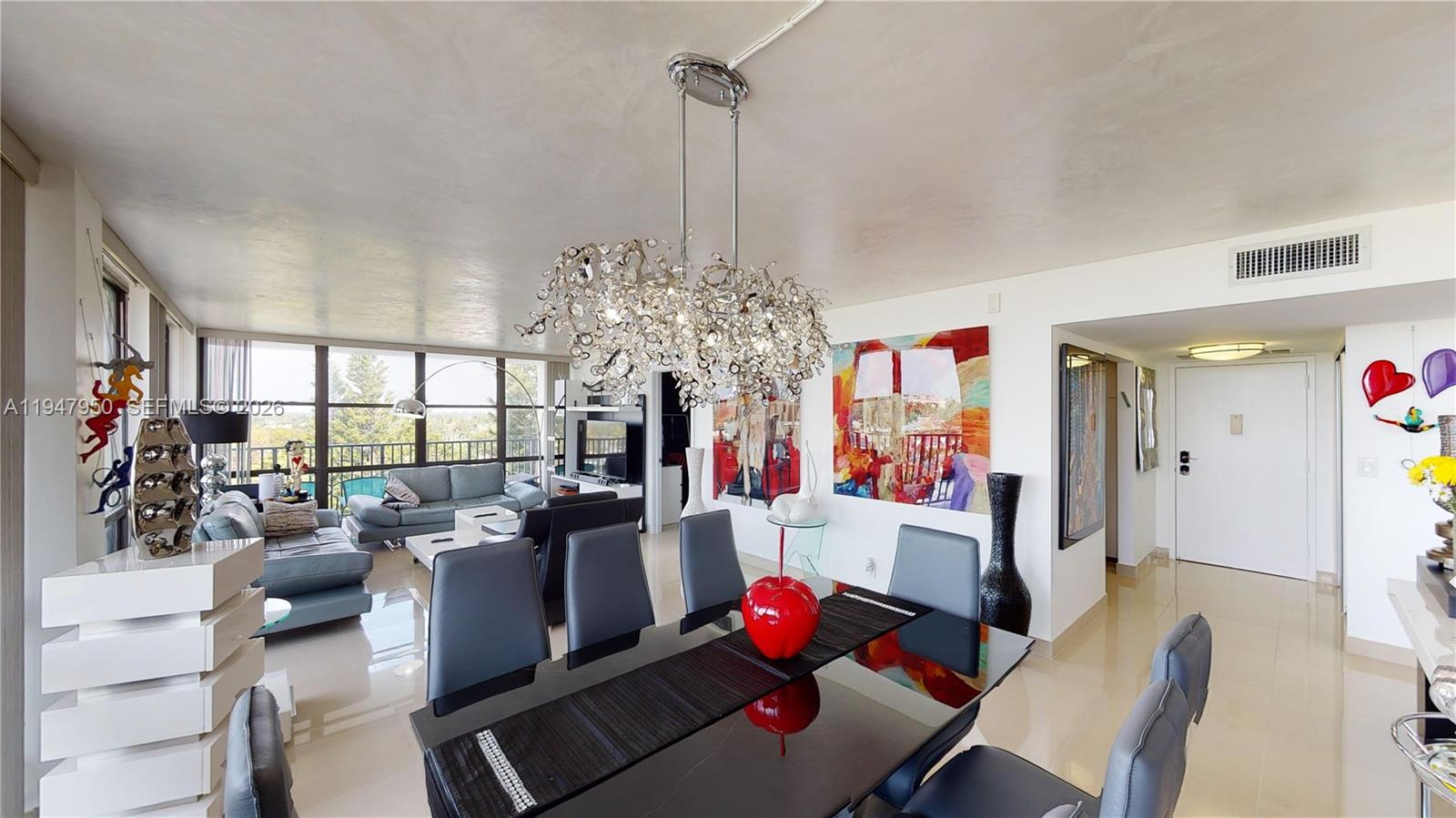 A dining area with a glass table and crystal chandelier opens into a living room — 800 Parkview Dr # 709, Hallandale Beach FL 33009, HALLANDALE BEACH, FL