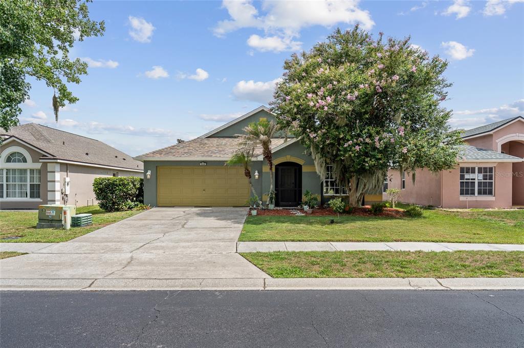 A single-story house with a tan garage, a front porch, and a large flowering tree — 3049 MERLOT WAY, CLERMONT, FL